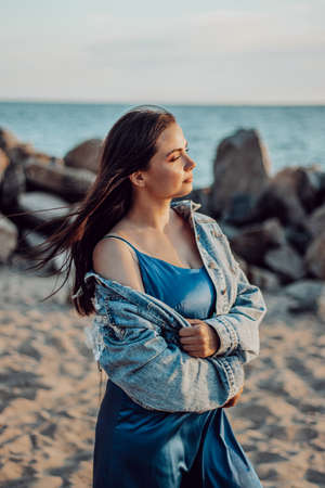 Beautiful girl with long dark hair walks on the beach in the evening and enjoys the sunset.の写真素材