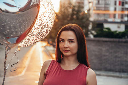 Portrait of a beautiful brunette with balloons at sunset in the city.の写真素材