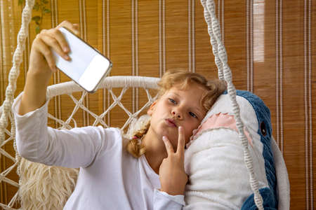 A girl with blond hair takes a selfie on a mobile phone with a toy sharkの写真素材