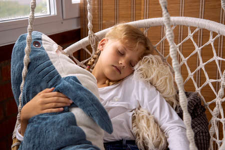 The girl sleeps in a hammock with a plush toy. Toy sharkの写真素材