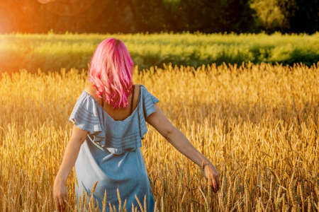 Girl with pink hair walking in a wheat fieldの写真素材