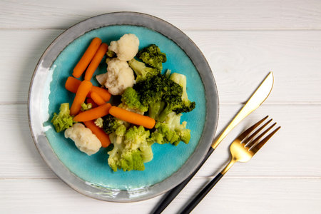 Steamed vegetables in a plate on a white wooden background, top viewの写真素材