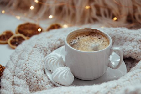 A cup of coffee with meringues and a knitted sweater - the concept of comfort and warmth. High...