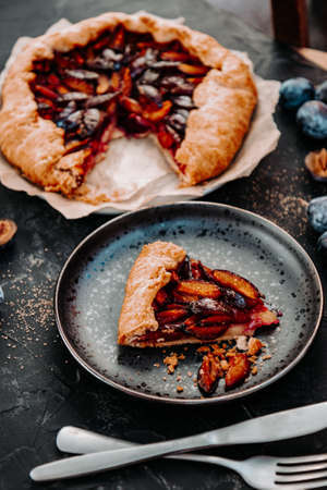 A piece of homemade plum pie on a black plate. Simple dessert with fruits, vertical photo. High quality photoの写真素材