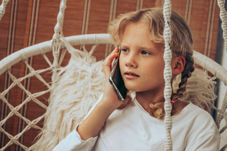 Girl talking on a cell phone while sitting in a chair on the balcony. High quality photoの写真素材
