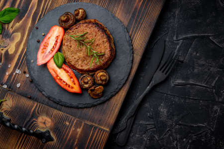 Meat cutlet with mushrooms and rosemary on a slate plate and a black background. Free space for your text. High quality photoの写真素材