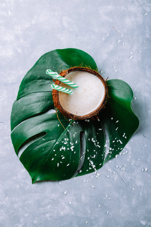 Coconut milk in coconut shell on green monstera leaf. High quality photo