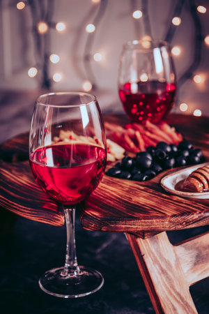 Two glasses of red wine and snacks - olives, meat and cheese on a board. Selective focus, vertical...
