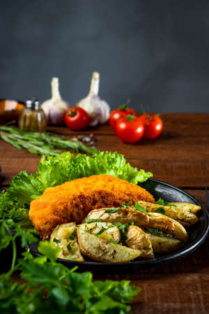 Pork schnitzel with baked potatoes in a frying pan on a wooden table close-up, vertical photoの写真素材