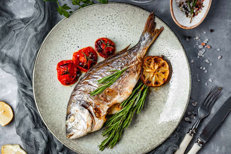 Baked dorado fish on a plate with vegetables top viewの写真素材