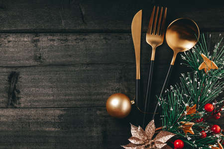 Golden cutlery and christmas ball on black wooden background, concept of new year table setting in minimal style. Free space for textの写真素材