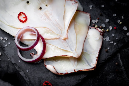 Raw peeled squid and spices for cooking on a slate board and black background. Close-up. High...