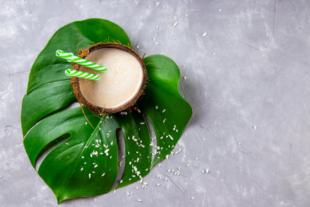 Coconut milk in coconut shell on green monstera leaf on the gray background, photo with copyspaceの写真素材