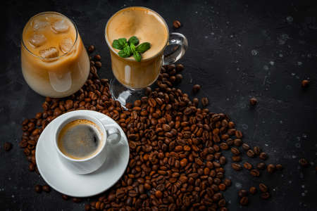 Cup of black coffee, a glass of ice coffee, a glass of latte and roasted coffee beans on the dark gray background. High quality photoの写真素材