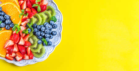 Web banner with fresh summer salad of various fruits and berries. Kiwi, orange, strawberry and blueberry on a plate decorated with mint on an yellow backgroundの写真素材