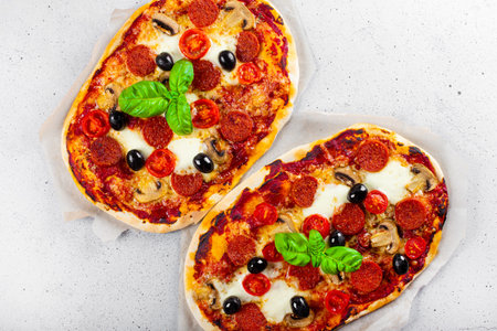 Two fresh homemade italian pizzas with mozzarella, pepperoni sausages, olives and basil top view