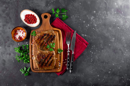 Two beef steaks cooked on the grill on a wooden cutting board on the dark gray background top view...