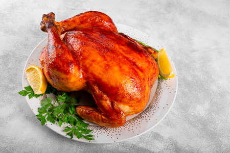 Whole baked chicken in sauce with paprika on a plate and light gray backgroundの写真素材