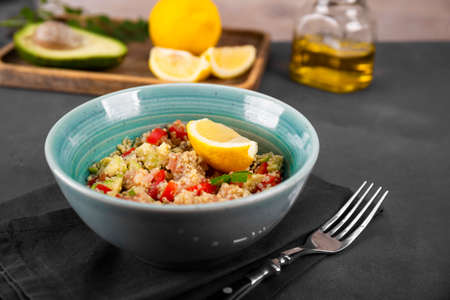 Salmon salad with tomatoes, avocado and quinoa in a blue bowl on a dark gray table, a dish of balanced dietの写真素材