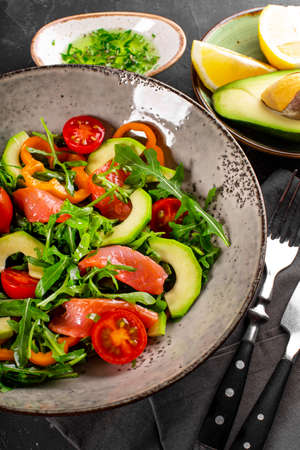Fresh summer vegetable salad with arugula, tomatoes, bell peppers, avocado and salmon on a plate close up vertical photoの写真素材