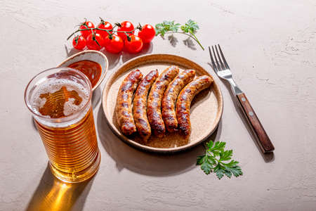 Grilled minced beef and pork sausages with barbecue sauce on a plate and a glass of beer on the table, photo with trending hard sunlight and shadowsの写真素材