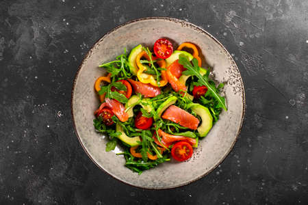 Fresh summer vegetable salad with arugula, tomatoes, bell peppers, avocado and salmon on a plate top view, photo with free space for textの写真素材