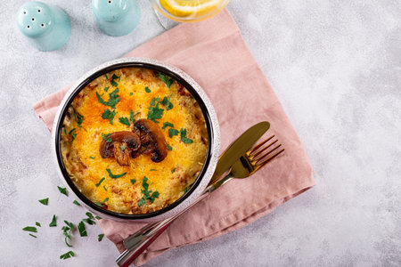 Julienne with potatoes and mushrooms in a baking dish on a light background, top view. Traditional...