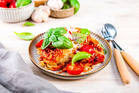 Italian pasta with tomato sauce, tomatoes, cheese and basil on a light tableの写真素材