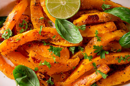 Baked pumpkin with basil and herbs on a white oval dish close-up. Autumn Vegetable Dishesの写真素材