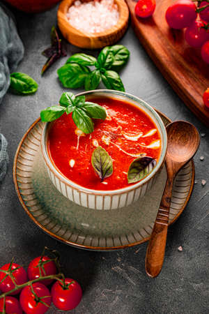 A bowl of traditional Spain tomato soup with cream and basil on the table vertical photo. Tomato and basil gazpacho in a gray bowlの写真素材