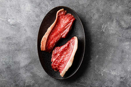Raw marbled beef steaks on the black plate and dark gray background, top view. Raw beef meat on the kitchen table. High quality photoの写真素材