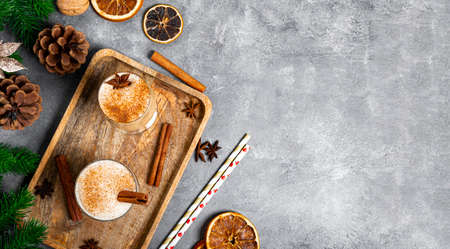 Two glasses of traditional Christmas drink eggnog on a gray background, web banner with copy space for text. Spicy drink made from egg and milk with cinnamon, cardamom.の写真素材