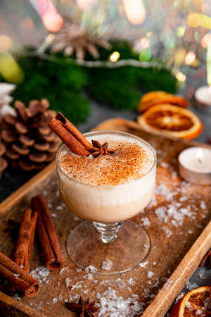 A glass of traditional Christmas drink eggnog on a festive table, vertical photo. Spicy drink made from egg and milk with cinnamon, cardamom.の写真素材