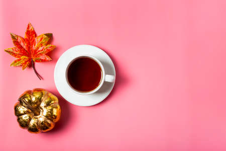 A cup of tea, autumn leave and golden pumpkin on the pink background top view. The concept of a cozy autumn at home with copy space for text. High quality photoの写真素材