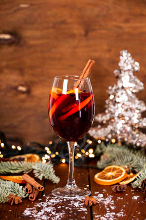 A glass of mulled wine on the wooden table surrounded by Christmas decorations. Festive winter drink vertical photoの写真素材