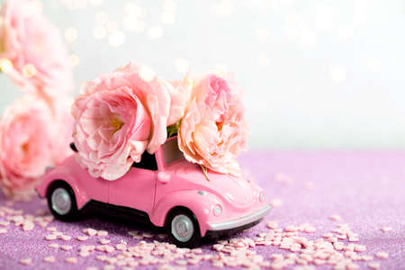 Pink retro car carries a bouquet of pink roses. Festive card with flowers, copy space for textの写真素材