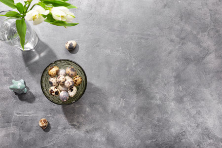 Quail eggs on the bowl and white spring flowers on the gray background, top view, free space for...