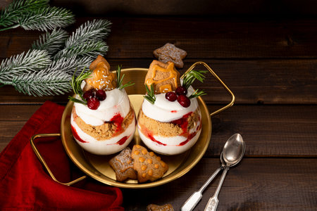 Two glasses of Christmas dessert with gingerbread cookies, whipped cream and cranberries on dark wooden background. High quality photoの写真素材