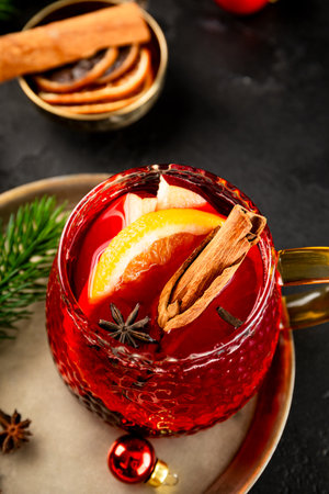 A glass mug of mulled wine on the black background and Christmas decorations. Festive winter drink, vertical photo. High quality photoの写真素材