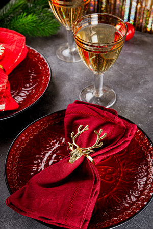 Christmas table setting, napkin with gold ring deer on red plate and two glasses of champagne on the table vertical photo. High quality photoの写真素材