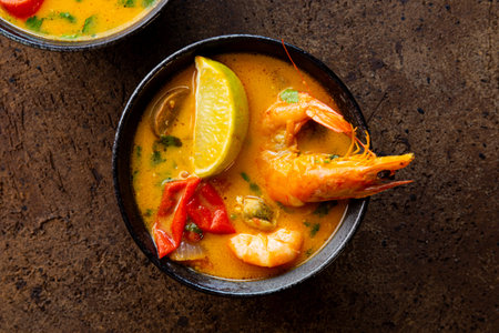 Tom yum soup with shrimp, sea food and lime on dark brown background top view. High quality photo
