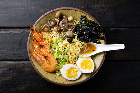 Asian ramen with shrimp, mushrooms, egg and greens on dark wooden background top viewの写真素材