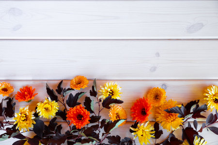 floral autumn background, leaves and yellow autumn flowers on white wooden background, copy space for text. High quality photoの写真素材