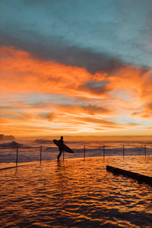 Surfer walking out to beach at sunrise