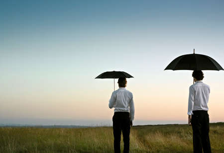 Two men with a black umbrella in an open, green field の写真素材