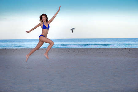 Young cheerful woman in bikini jumping on the beach.の写真素材