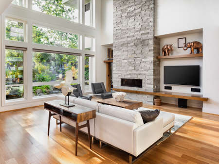 living room interior with hardwood floors, fireplace, and large bank of windows with view of lush vegetation, in new luxury homeの写真素材