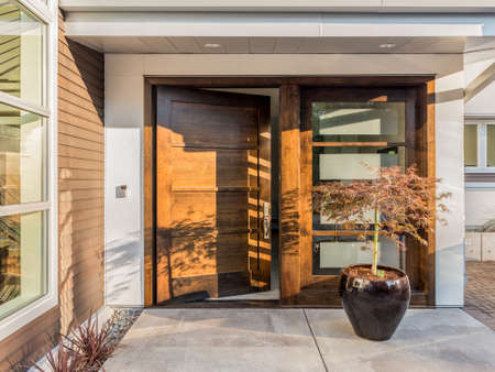 Beautiful Wood Door as Entrance to New Luxury Home: Large and Wide Hardwood Door with Windows and Potted Plant to Right of Door in Exterior of Beautiful House. Cement Patio. Door is Slightly AjarOpenの写真素材