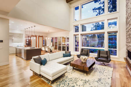 large living room with vaulted ceilings in new luxury home, with large bank of windows, view of kitchen and furnishings