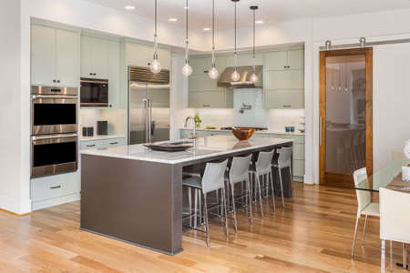 Kitchen Interior with Island, Sink, Cabinets, and Hardwood Floors in New Luxury Home with Lights Onの写真素材